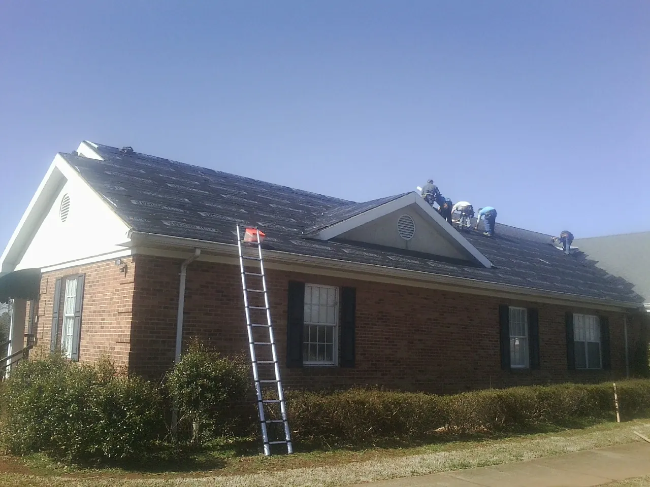 Crew tearing shingles off a brick ranch roof with a ladder set — Emergency Roof Repair work by our crew in Mount Hermon