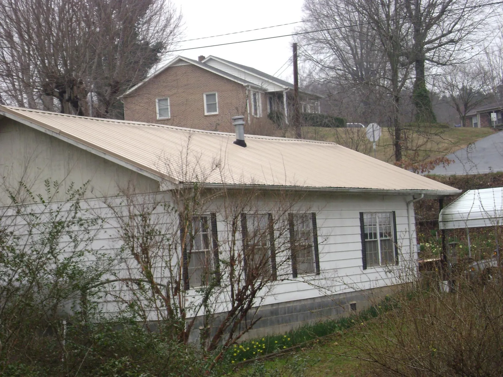 Tan metal roof on a white sided house set into a hillside — Commercial Roofing by Roofing Brothers in Mount Hermon