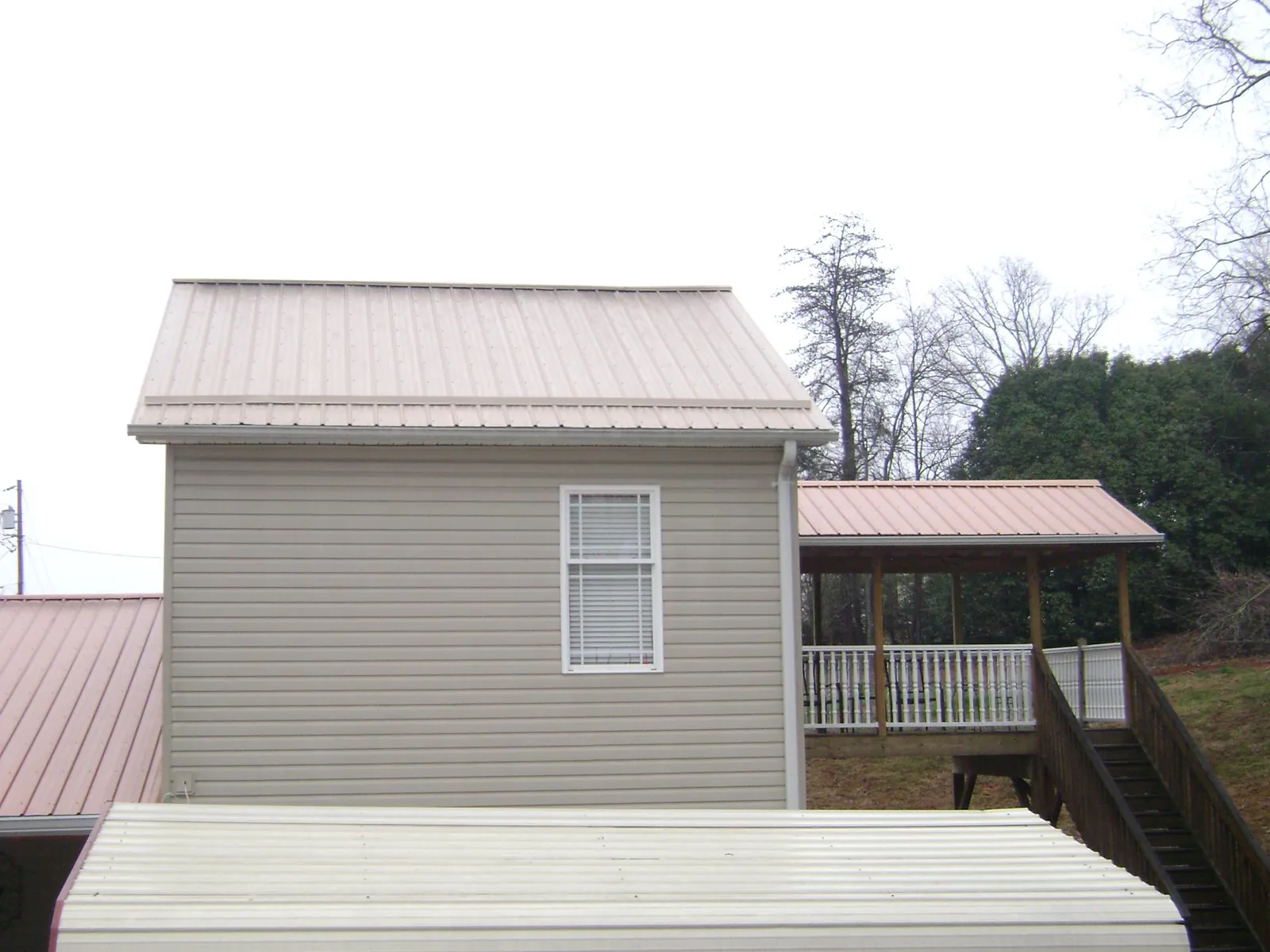 Tan metal roofs on a two story addition and attached porch, from a Roof Replacement job in Mount Hermon
